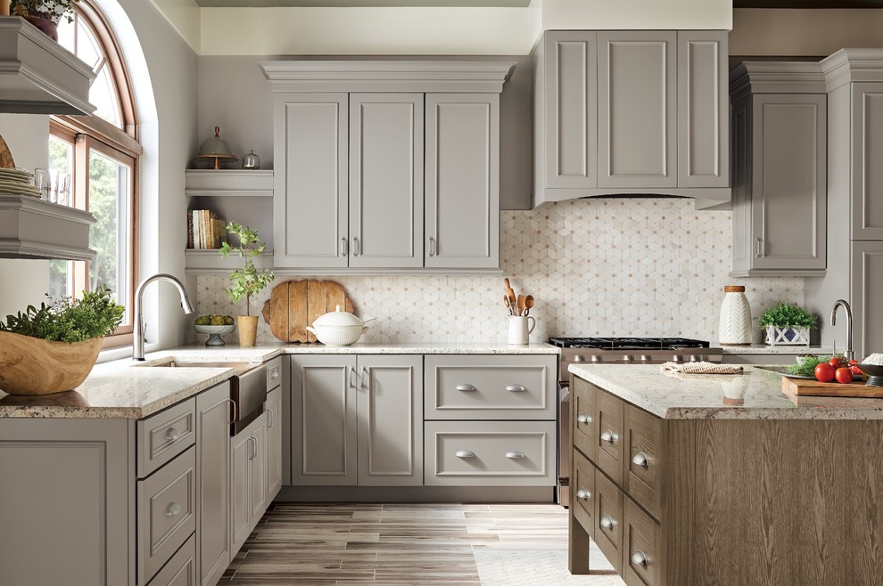 Inredning av ett klassiskt mellanstort grå grått kök, med en rustik diskho, luckor med profilerade fronter, grå skåp, granitbänkskiva, vitt stänkskydd, rostfria vitvaror, vinylgolv, en köksö och brunt golv