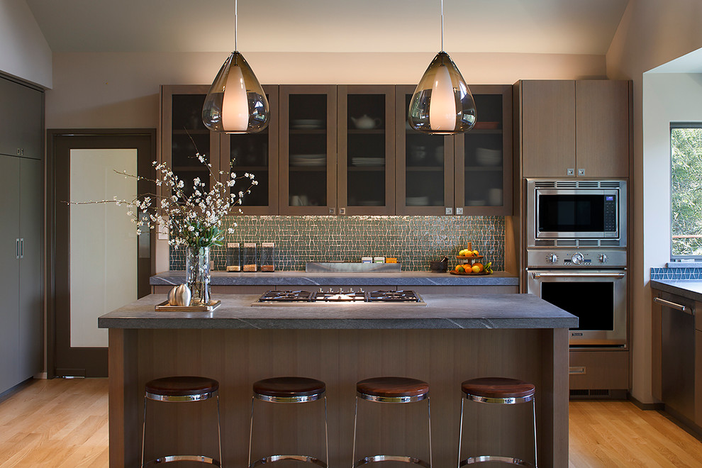 This is an example of a contemporary l-shaped kitchen in San Francisco with an island, glass-front cabinets, dark wood cabinets, green splashback, stainless steel appliances and medium hardwood flooring.