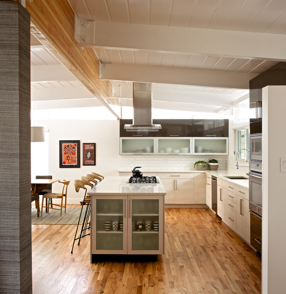Exempel på ett mellanstort modernt kök, med en undermonterad diskho, luckor med glaspanel, vita skåp, vitt stänkskydd, stänkskydd i tunnelbanekakel, mellanmörkt trägolv, en köksö, bänkskiva i koppar och rostfria vitvaror
