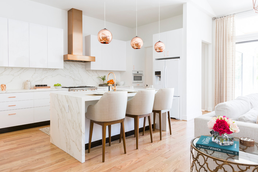 Contemporary open plan kitchen in Houston with flat-panel cabinets, white cabinets, marble worktops, white splashback, marble splashback, white appliances, light hardwood flooring and an island.