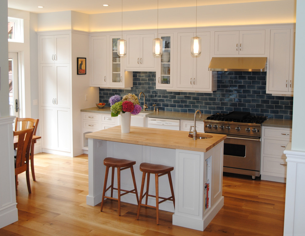 This is an example of a medium sized traditional l-shaped kitchen/diner in San Francisco with a belfast sink, shaker cabinets, white cabinets, wood worktops, blue splashback, metro tiled splashback, stainless steel appliances, medium hardwood flooring and an island.