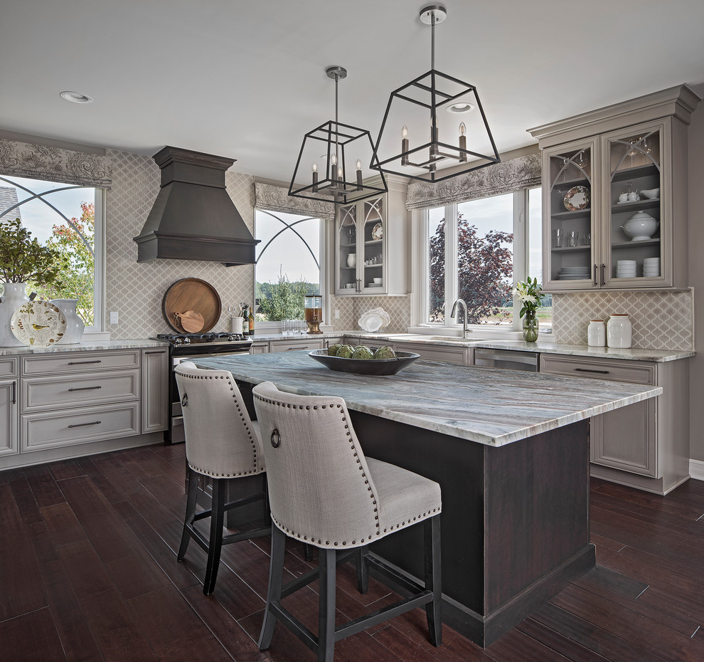 This is an example of a traditional l-shaped kitchen/diner in Other with glass-front cabinets, grey cabinets, stainless steel appliances, an island, brown floors, a submerged sink, grey splashback and dark hardwood flooring.