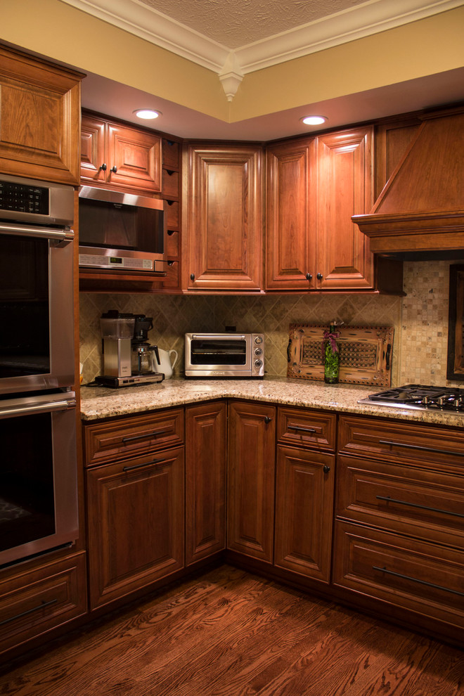 Example of a mid-sized u-shaped medium tone wood floor eat-in kitchen design in Other with an integrated sink, raised-panel cabinets, medium tone wood cabinets, granite countertops, beige backsplash, stainless steel appliances and an island