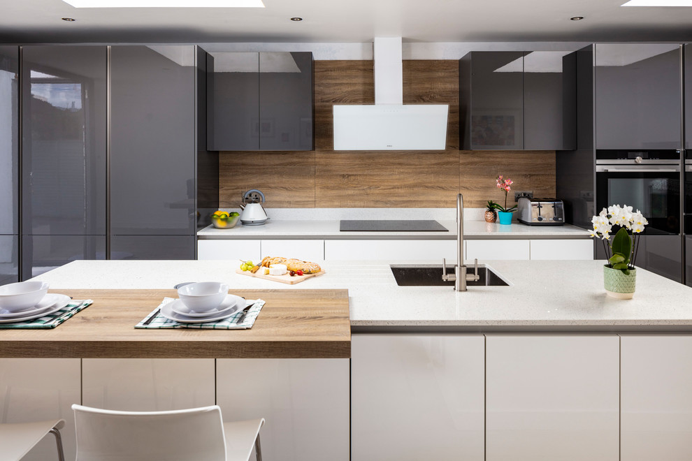 Exempel på ett modernt vit vitt kök och matrum, med en integrerad diskho, släta luckor, grå skåp, bänkskiva i kvartsit, brunt stänkskydd, stänkskydd i trä, svarta vitvaror, ljust trägolv, en halv köksö och brunt golv