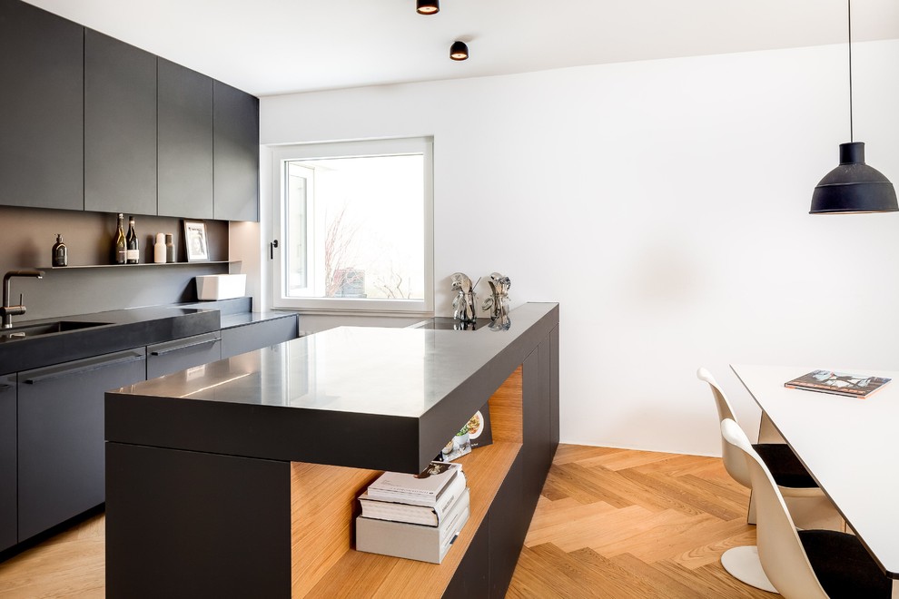 Inspiration for a medium sized scandi single-wall kitchen/diner in Munich with a built-in sink, flat-panel cabinets, black cabinets, black splashback, medium hardwood flooring, an island and brown floors.