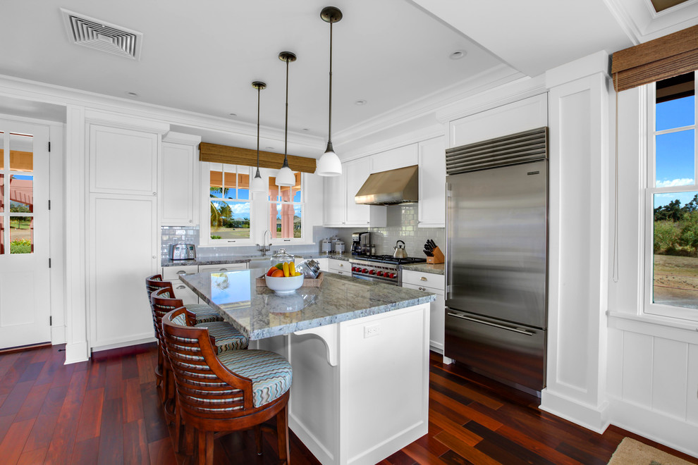 Foto di un cucina con isola centrale tropicale con ante bianche, top in granito, paraspruzzi bianco, paraspruzzi con piastrelle in ceramica e pavimento in legno massello medio