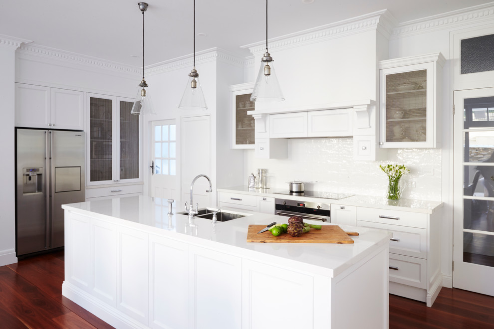 Exempel på ett stort klassiskt u-kök, med en dubbel diskho, luckor med infälld panel, vita skåp, vitt stänkskydd, stänkskydd i keramik, rostfria vitvaror, mellanmörkt trägolv och en köksö
