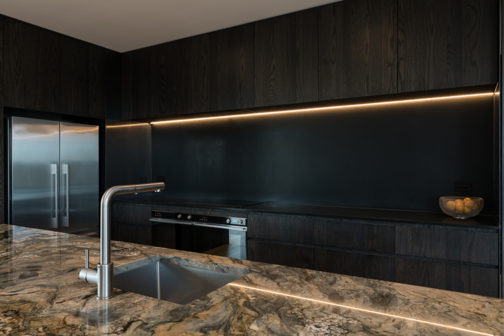 This is an example of a medium sized urban galley kitchen/diner in Auckland with a single-bowl sink, flat-panel cabinets, dark wood cabinets, marble worktops, black splashback, slate splashback, stainless steel appliances, light hardwood flooring, an island, brown floors and black worktops.