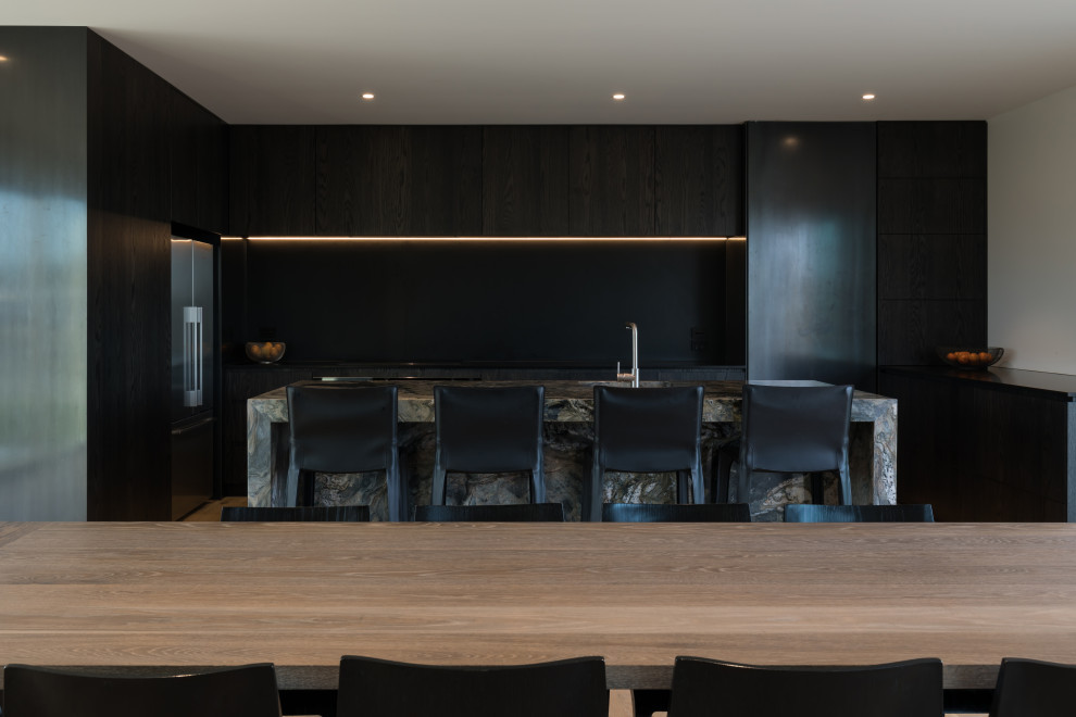 Foto på ett mellanstort industriellt svart kök, med en enkel diskho, släta luckor, skåp i mörkt trä, marmorbänkskiva, svart stänkskydd, stänkskydd i skiffer, rostfria vitvaror, ljust trägolv, en köksö och brunt golv