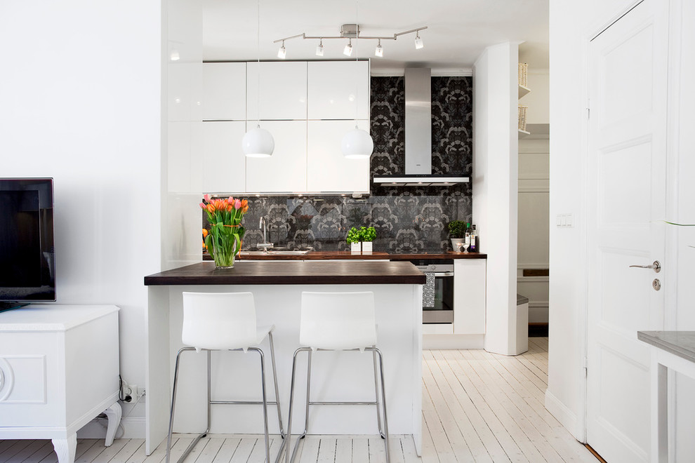 Inspiration for a medium sized scandinavian single-wall kitchen/diner in Stockholm with a submerged sink, flat-panel cabinets, white cabinets, black splashback, stainless steel appliances, painted wood flooring, wood worktops and an island.