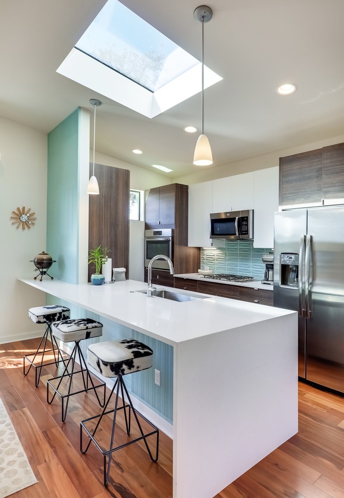 Inspiration for a retro galley open plan kitchen in Austin with a submerged sink, flat-panel cabinets, dark wood cabinets, blue splashback, stainless steel appliances, medium hardwood flooring, a breakfast bar and brown floors.