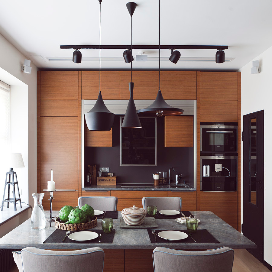 Cette image montre une cuisine ouverte design en bois brun avec un placard à porte plane, une crédence noire, un électroménager noir et îlot.