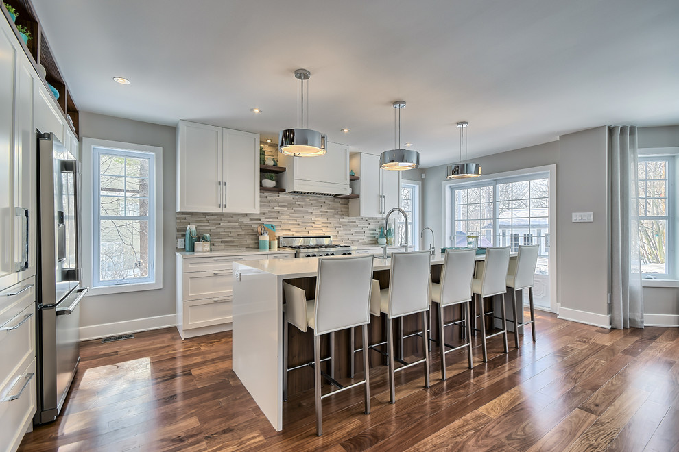 Medium sized traditional l-shaped kitchen/diner in Montreal with a submerged sink, shaker cabinets, white cabinets, engineered stone countertops, grey splashback, stone tiled splashback, stainless steel appliances, medium hardwood flooring and an island.