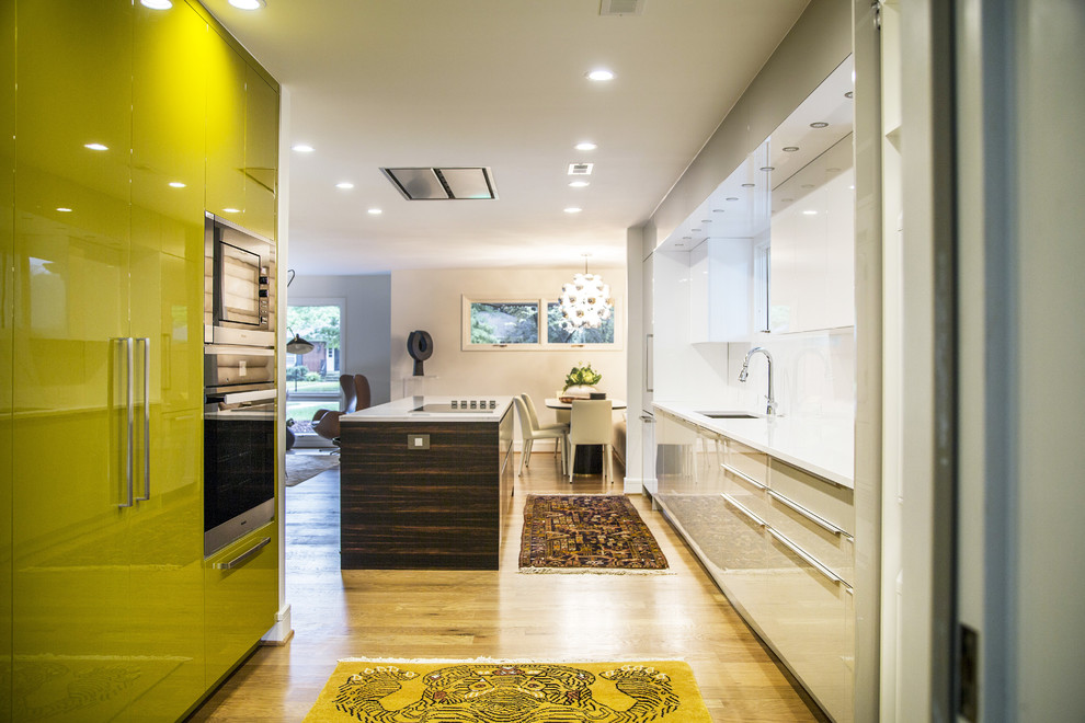 Photo of a contemporary galley open plan kitchen in Charlotte with a submerged sink, flat-panel cabinets, green cabinets, white splashback, integrated appliances, medium hardwood flooring, an island, brown floors and white worktops.