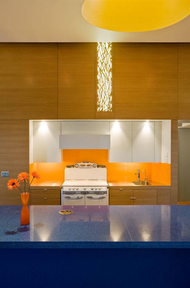 Modelo de cocina actual con fregadero integrado, salpicadero naranja, electrodomésticos blancos y encimeras azules