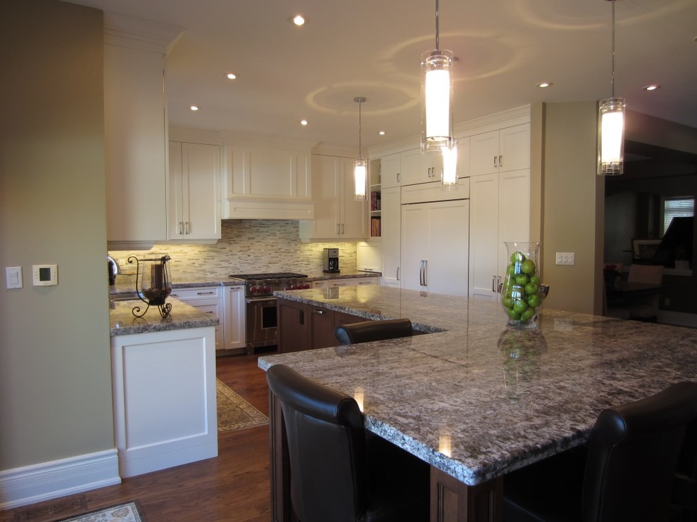 Example of a classic u-shaped medium tone wood floor eat-in kitchen design in Toronto with an undermount sink, recessed-panel cabinets, white cabinets, granite countertops, beige backsplash, stone tile backsplash, paneled appliances and an island