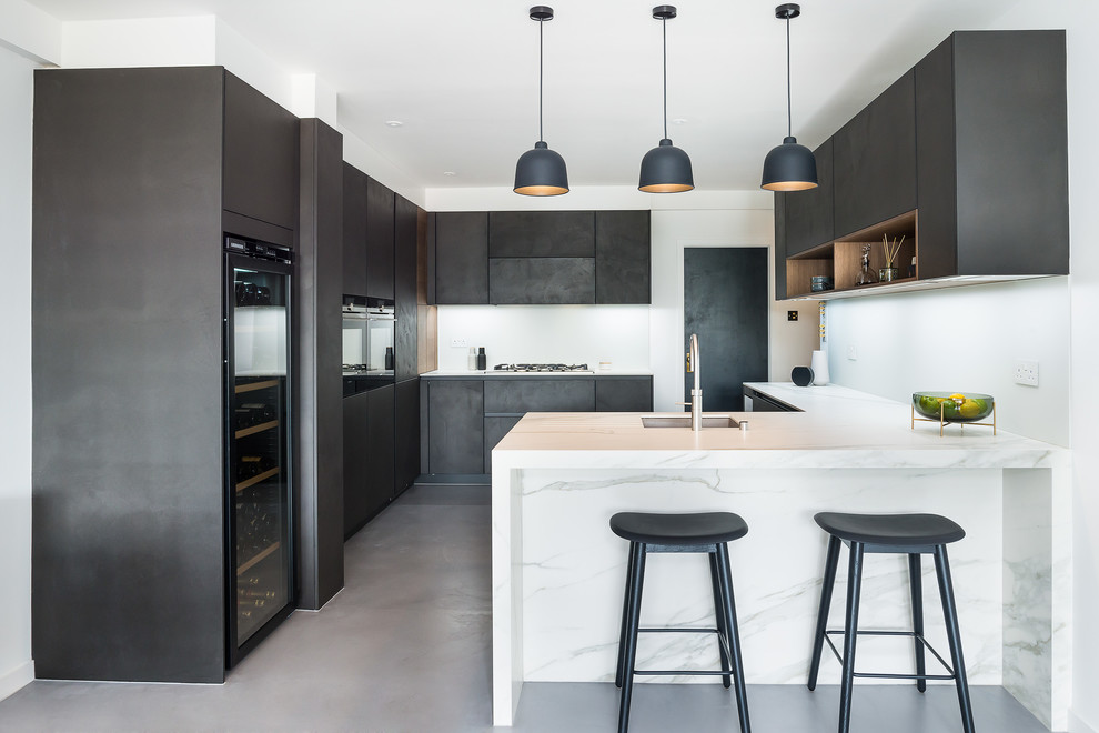 Идея дизайна: п-образная кухня среднего размера в современном стиле с врезной мойкой, плоскими фасадами, черными фасадами, бетонным полом, полуостровом, серым полом и белой столешницей