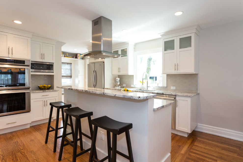 Foto på ett mellanstort retro kök, med en enkel diskho, luckor med infälld panel, vita skåp, granitbänkskiva, grått stänkskydd, stänkskydd i keramik, rostfria vitvaror, mellanmörkt trägolv och en köksö