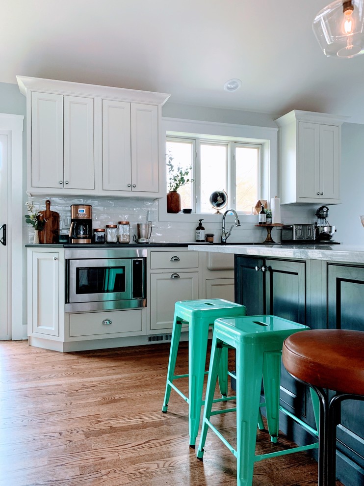 Example of a mid-sized trendy l-shaped medium tone wood floor and brown floor eat-in kitchen design in Chicago with a farmhouse sink, beaded inset cabinets, white cabinets, quartzite countertops, white backsplash, subway tile backsplash, stainless steel appliances, an island and white countertops