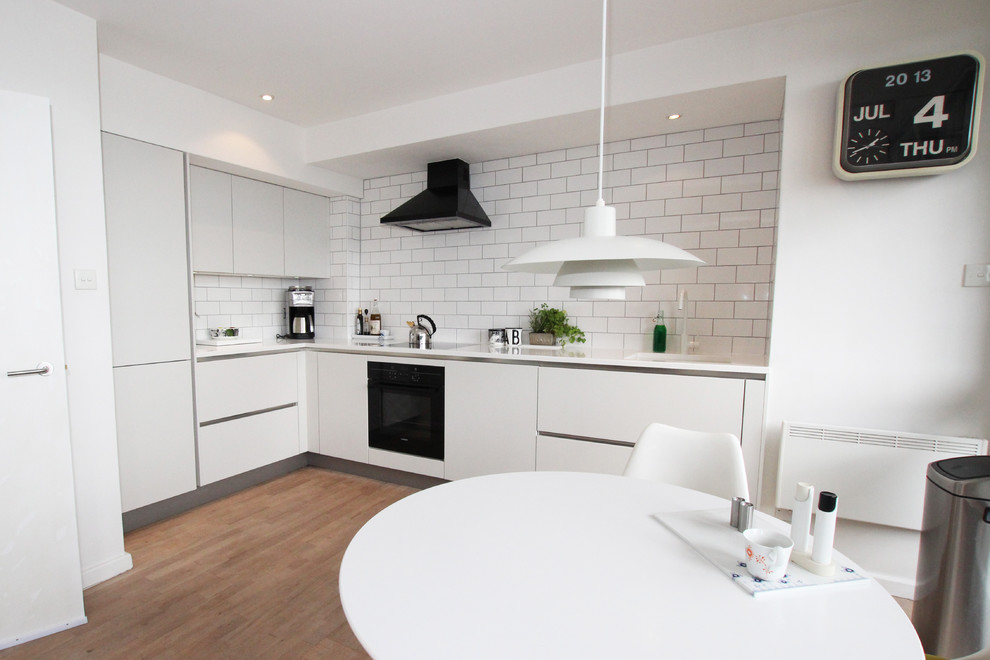 Küche in L-Form mit weißen Schränken, Rückwand aus Mosaikfliesen und weißen Elektrogeräten in London