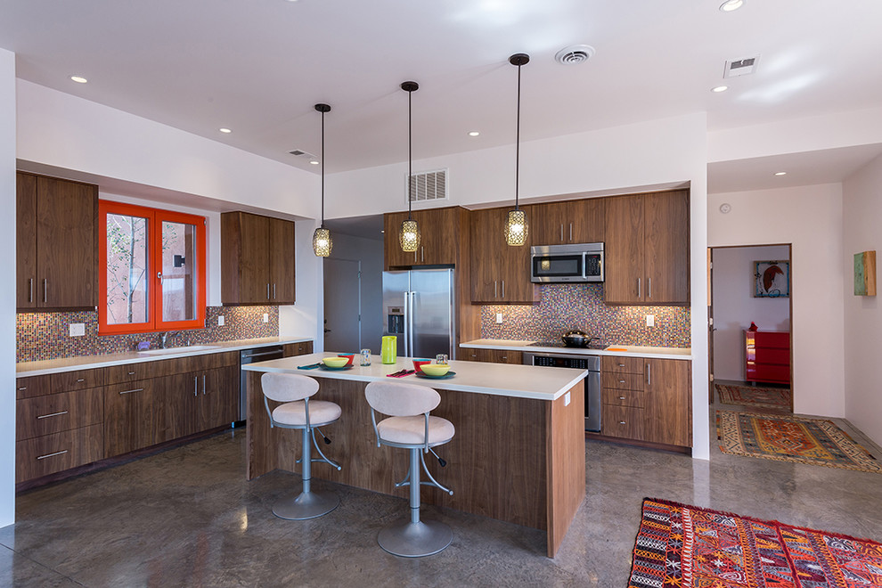 Photo of a medium sized contemporary l-shaped open plan kitchen in Albuquerque with flat-panel cabinets, an island, medium wood cabinets, glass tiled splashback, stainless steel appliances, concrete flooring, a submerged sink, engineered stone countertops, multicoloured worktops and grey floors.