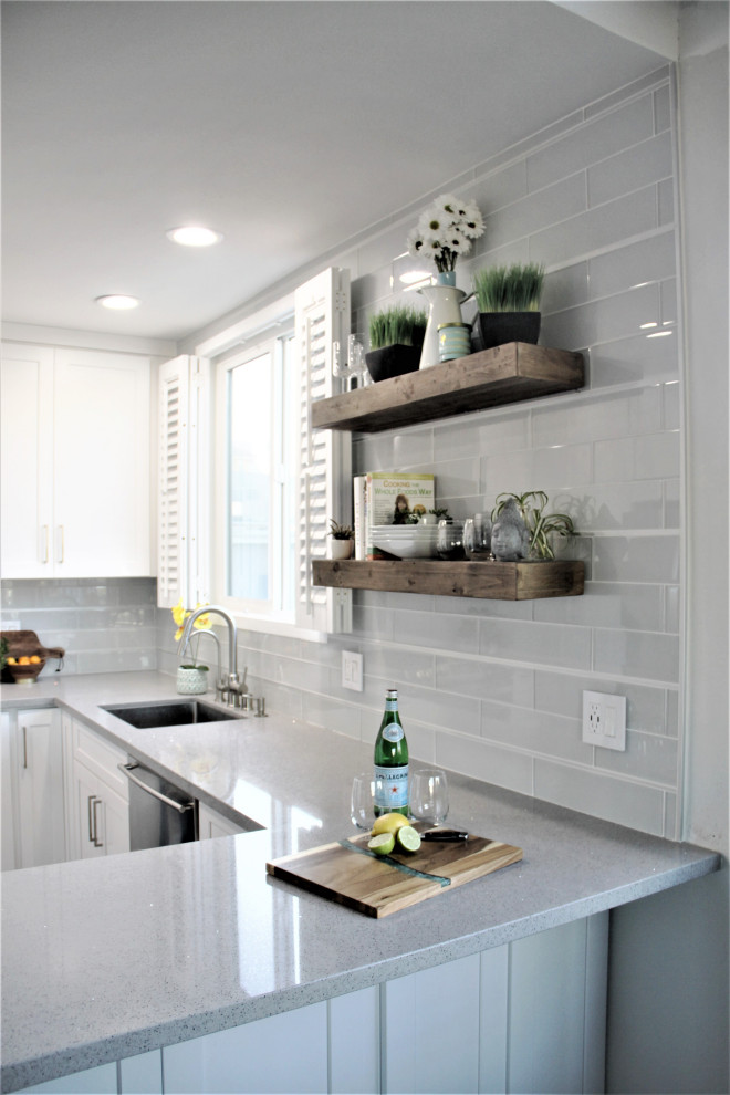 Small beach style grey and white u-shaped kitchen/diner in Atlanta with a submerged sink, shaker cabinets, white cabinets, engineered stone countertops, white splashback, glass tiled splashback, stainless steel appliances, laminate floors, a breakfast bar, brown floors and grey worktops.