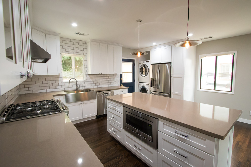 Photo of a medium sized contemporary l-shaped open plan kitchen in Los Angeles with a submerged sink, shaker cabinets, white cabinets, engineered stone countertops, white splashback, metro tiled splashback, stainless steel appliances, dark hardwood flooring, an island and brown floors.