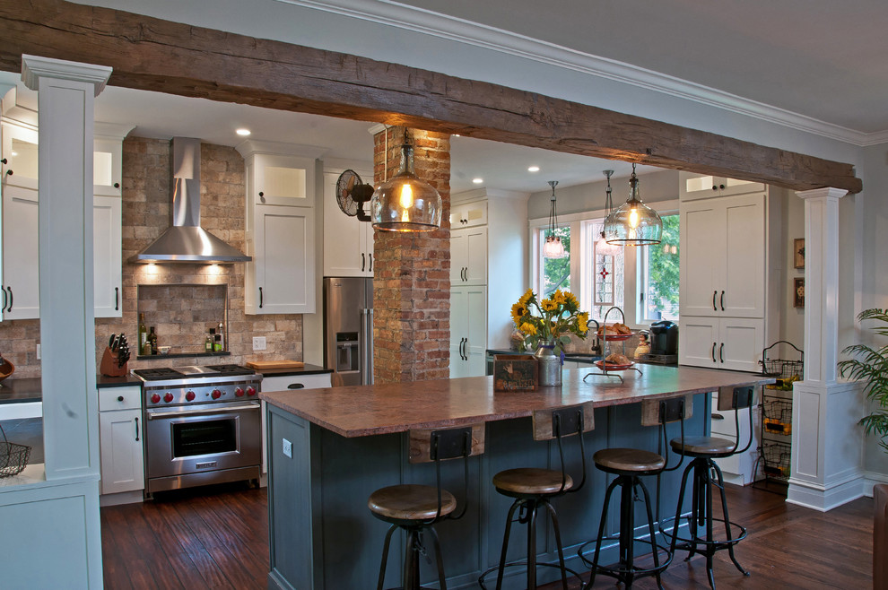 Inspiration for a large cottage l-shaped medium tone wood floor and brown floor eat-in kitchen remodel in Chicago with shaker cabinets, stainless steel appliances, an island, white cabinets, a farmhouse sink, soapstone countertops, stone tile backsplash and brown backsplash