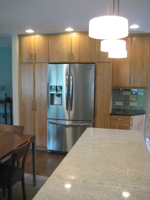 Bild på ett mellanstort funkis linjärt kök och matrum, med släta luckor, skåp i mellenmörkt trä, granitbänkskiva, grönt stänkskydd, stänkskydd i tunnelbanekakel, rostfria vitvaror, mellanmörkt trägolv och en köksö