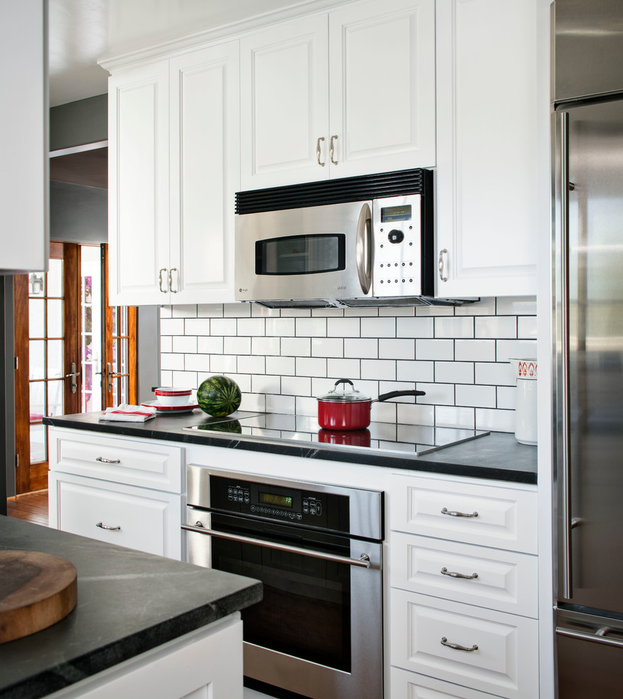 Inspiration for a mid-sized coastal u-shaped medium tone wood floor enclosed kitchen remodel in San Francisco with a farmhouse sink, white cabinets, soapstone countertops, white backsplash, subway tile backsplash, stainless steel appliances, no island and recessed-panel cabinets