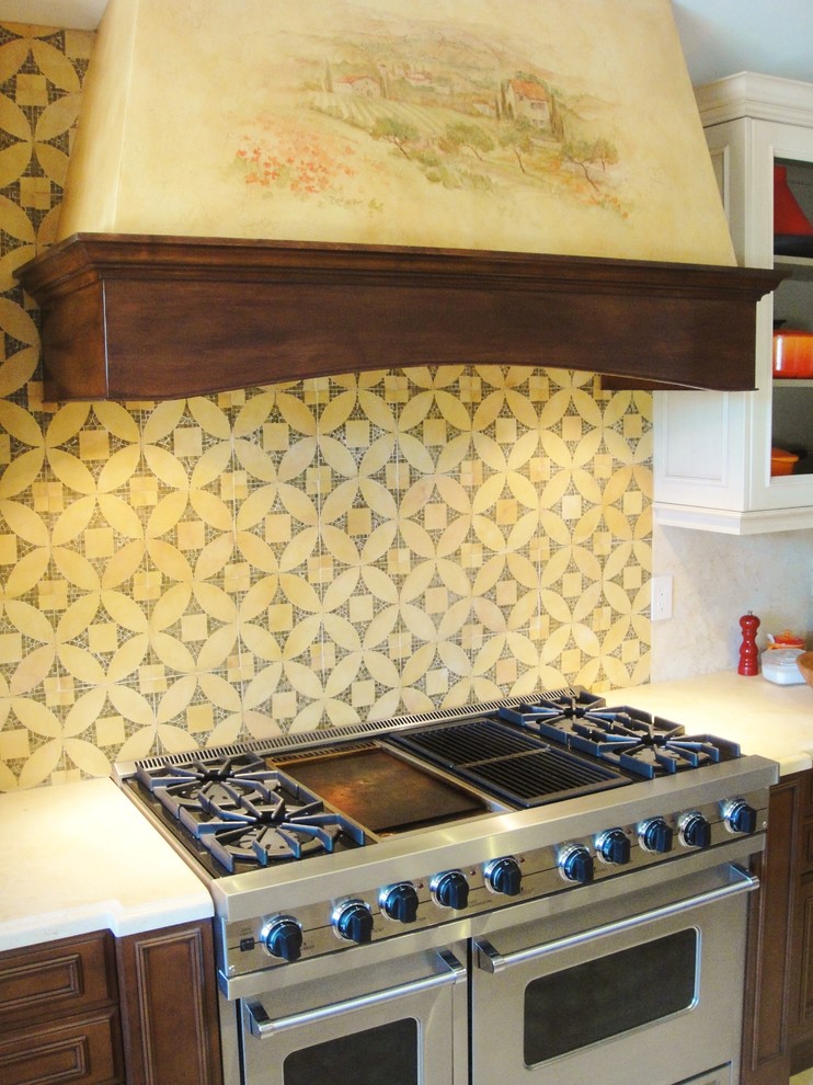 Inredning av ett klassiskt mellanstort kök, med en undermonterad diskho, luckor med profilerade fronter, skåp i mellenmörkt trä, bänkskiva i kalksten, gult stänkskydd, stänkskydd i mosaik, integrerade vitvaror, klinkergolv i porslin och en köksö