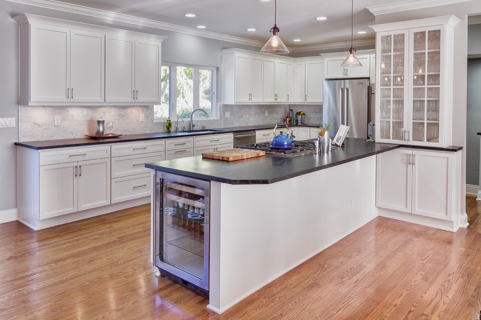 Elegant u-shaped eat-in kitchen photo in San Diego with a drop-in sink, glass-front cabinets, white cabinets, granite countertops, gray backsplash, subway tile backsplash and stainless steel appliances