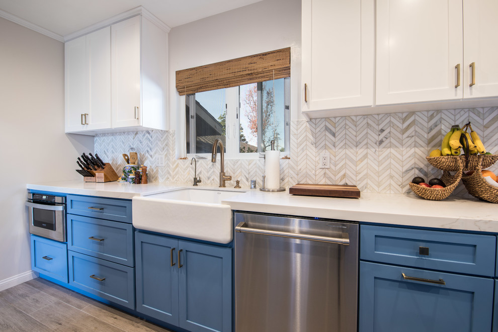 Inspiration for a mid-sized transitional galley light wood floor and brown floor open concept kitchen remodel in Los Angeles with a farmhouse sink, shaker cabinets, blue cabinets, quartzite countertops, beige backsplash, ceramic backsplash, stainless steel appliances, no island and white countertops