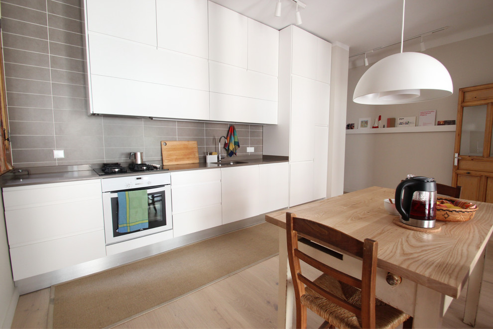 Einzeilige Moderne Wohnküche mit flächenbündigen Schrankfronten, weißen Schränken, Küchenrückwand in Grau und weißen Elektrogeräten in Madrid
