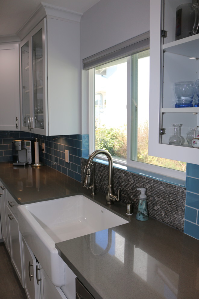 Design ideas for a medium sized contemporary u-shaped kitchen/diner in San Diego with a belfast sink, shaker cabinets, white cabinets, composite countertops, blue splashback, glass tiled splashback, stainless steel appliances, ceramic flooring and an island.