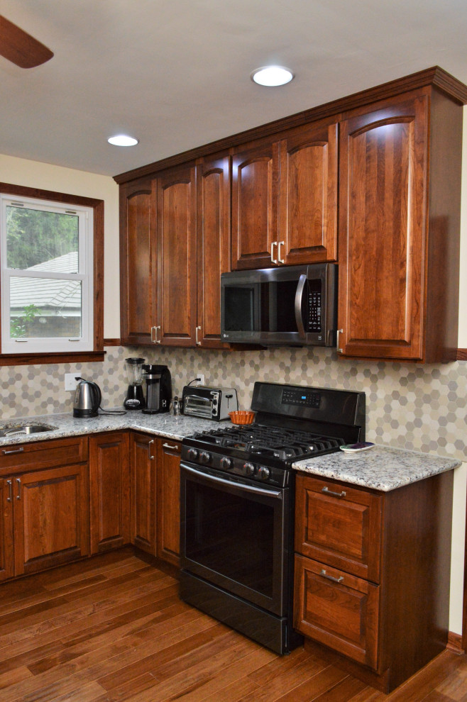 Amerikansk inredning av ett avskilt, stort flerfärgad flerfärgat l-kök, med en undermonterad diskho, luckor med upphöjd panel, skåp i mörkt trä, granitbänkskiva, flerfärgad stänkskydd, rostfria vitvaror, mellanmörkt trägolv och brunt golv