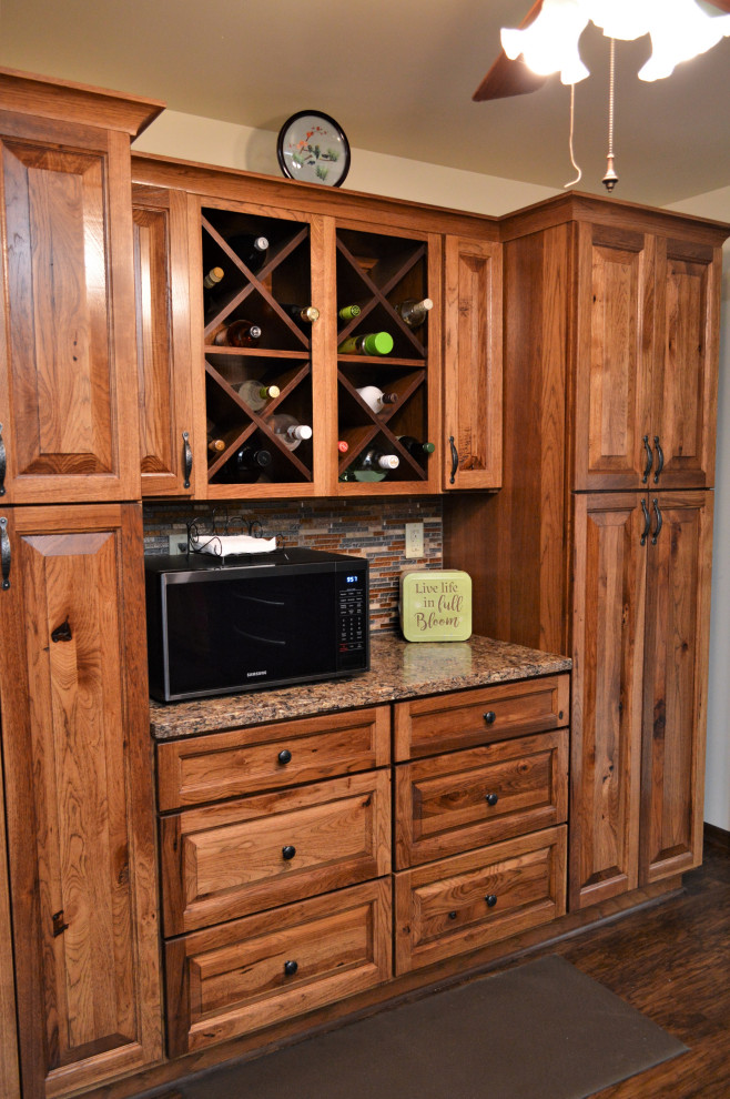Inredning av ett rustikt stort brun brunt kök, med en undermonterad diskho, luckor med upphöjd panel, skåp i mellenmörkt trä, bänkskiva i kvartsit, flerfärgad stänkskydd, stänkskydd i stickkakel, svarta vitvaror, laminatgolv, en köksö och brunt golv