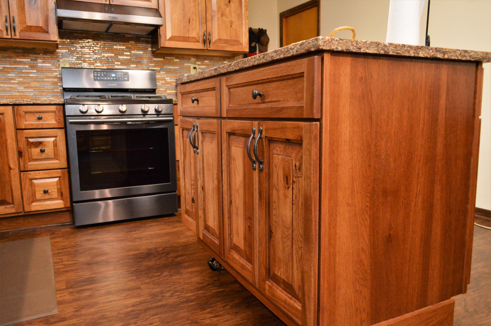 Foto på ett stort rustikt brun kök, med en undermonterad diskho, luckor med upphöjd panel, skåp i mellenmörkt trä, bänkskiva i kvartsit, flerfärgad stänkskydd, stänkskydd i stickkakel, svarta vitvaror, laminatgolv, en köksö och brunt golv