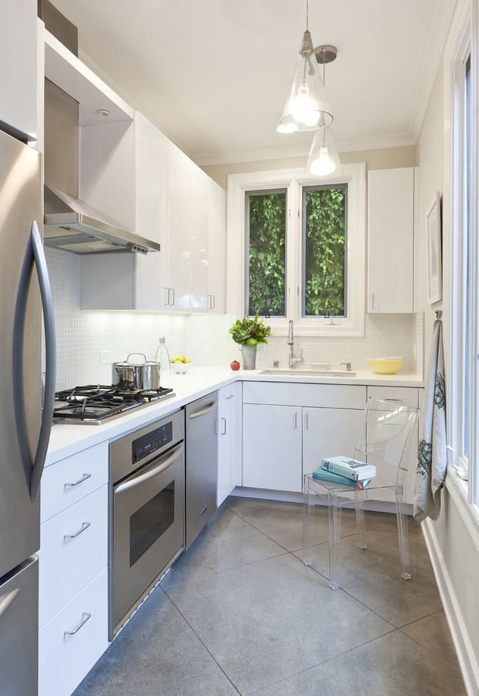 Bild på ett avskilt funkis l-kök, med rostfria vitvaror, en undermonterad diskho, släta luckor, vita skåp, vitt stänkskydd och stänkskydd i mosaik