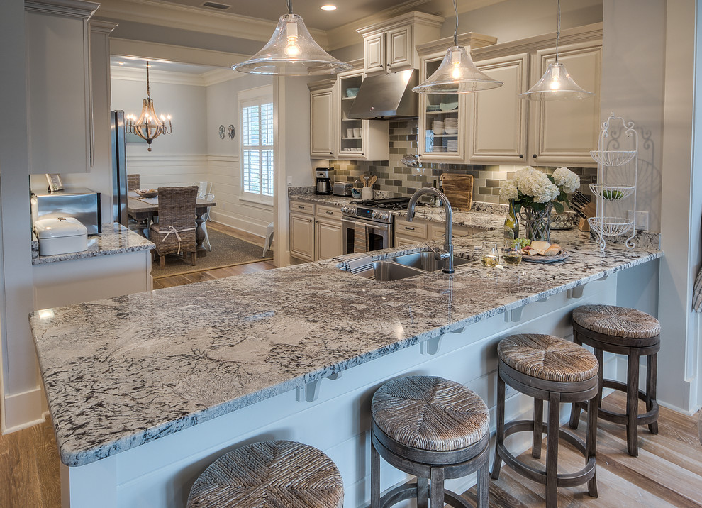 Nautical l-shaped kitchen in Miami with a double-bowl sink, raised-panel cabinets, white cabinets, grey splashback, stainless steel appliances, light hardwood flooring and a breakfast bar.