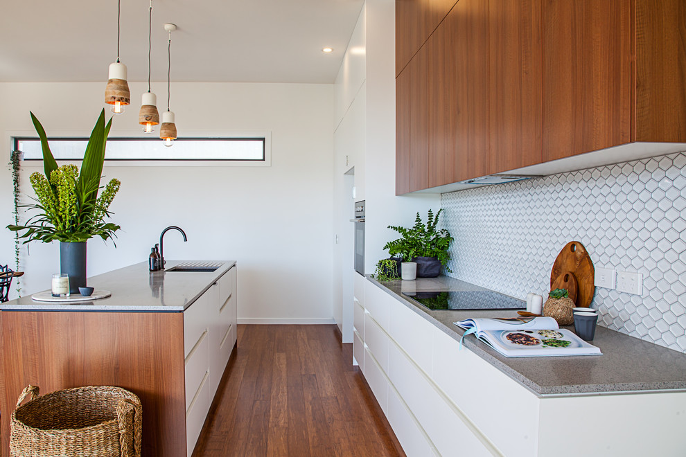 Zweizeilige, Mittelgroße Moderne Wohnküche mit flächenbündigen Schrankfronten, weißen Schränken, Laminat-Arbeitsplatte, Küchenrückwand in Weiß, Rückwand aus Keramikfliesen, weißen Elektrogeräten, braunem Holzboden, Kücheninsel und Unterbauwaschbecken in Hobart