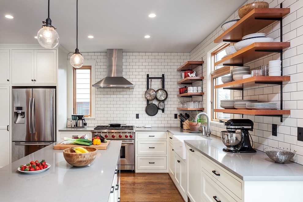 Eat-in kitchen - mid-sized cottage l-shaped dark wood floor and brown floor eat-in kitchen idea in Portland with a farmhouse sink, shaker cabinets, white cabinets, solid surface countertops, white backsplash, subway tile backsplash, stainless steel appliances and an island