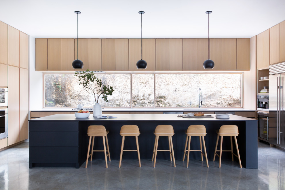 Immagine di un cucina con isola centrale moderno con ante lisce, ante in legno chiaro, paraspruzzi a finestra, elettrodomestici in acciaio inossidabile, pavimento in cemento, pavimento grigio e top bianco