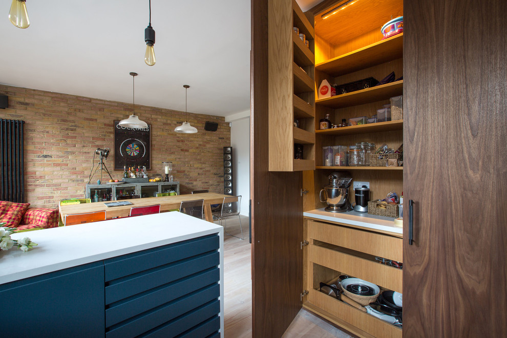 Photo of a medium sized eclectic l-shaped open plan kitchen in London with a built-in sink, flat-panel cabinets, blue cabinets, composite countertops, stainless steel appliances, light hardwood flooring and a breakfast bar.