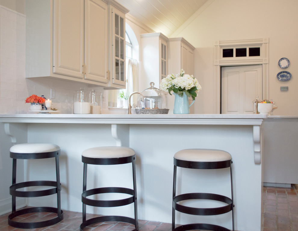 Mid-sized transitional l-shaped brick floor open concept kitchen photo in New Orleans with a farmhouse sink, raised-panel cabinets, white cabinets, marble countertops, white backsplash, porcelain backsplash, stainless steel appliances and an island