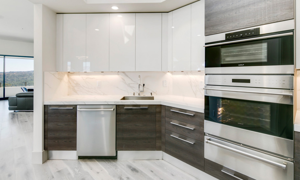 Inredning av ett modernt stort vit vitt kök, med en undermonterad diskho, släta luckor, grå skåp, bänkskiva i kvarts, vitt stänkskydd, rostfria vitvaror, ljust trägolv, en köksö och grått golv