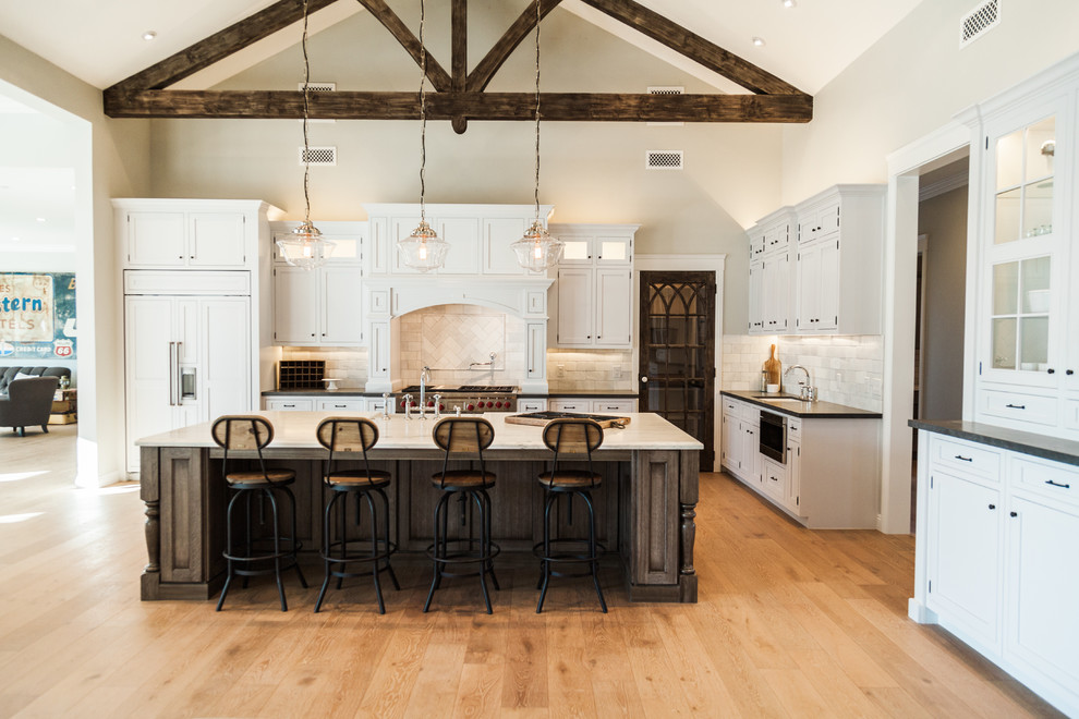 Large farmhouse l-shaped light wood floor open concept kitchen photo in Phoenix with a farmhouse sink, shaker cabinets, yellow cabinets, marble countertops, gray backsplash, stone tile backsplash, white appliances and an island