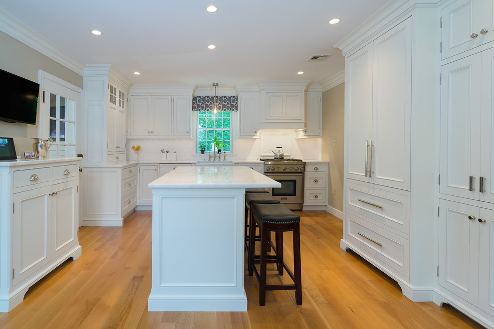Exempel på ett klassiskt vit vitt kök, med en rustik diskho, luckor med profilerade fronter, vita skåp, bänkskiva i kvartsit, vitt stänkskydd, stänkskydd i tunnelbanekakel, rostfria vitvaror, ljust trägolv, en köksö och brunt golv