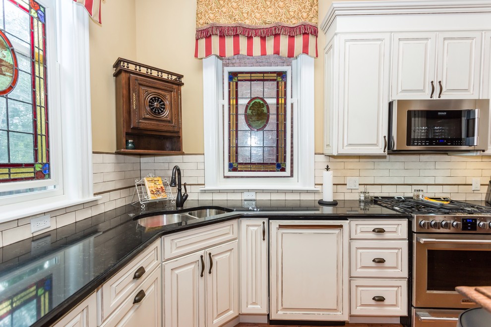 セントルイスにある広いヴィクトリアン調のおしゃれなキッチン (ダブルシンク、レイズドパネル扉のキャビネット、白いキャビネット、クオーツストーンカウンター、白いキッチンパネル、サブウェイタイルのキッチンパネル、シルバーの調理設備、無垢フローリング) の写真