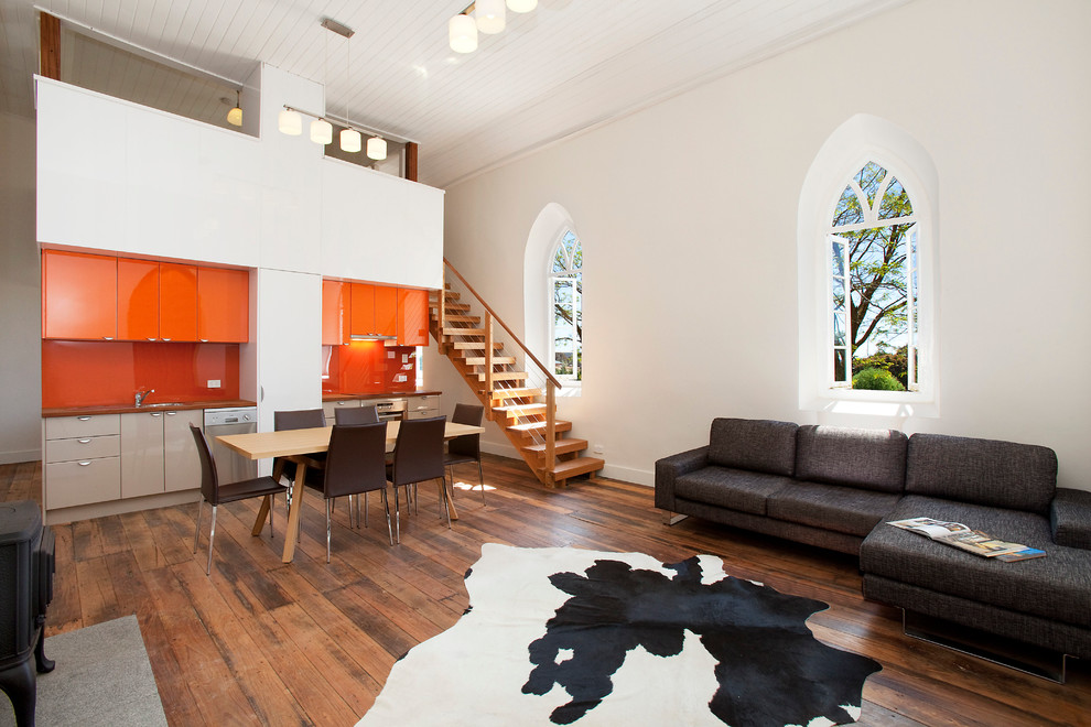 Photo of an industrial single-wall open plan kitchen in Sydney with a submerged sink, flat-panel cabinets, orange cabinets, orange splashback, glass sheet splashback and stainless steel appliances.